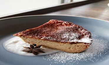 Slice of baked cheesecake served on a blue plate with powdered sugar and star anise.