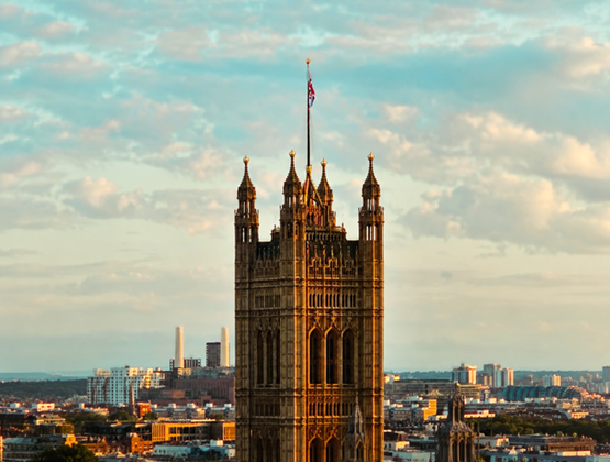 Elizabeth Tower at the Palace of Westminster in London, lit by the setting sun with the city skyline in the background.