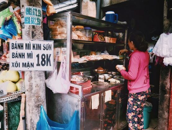 Stand de rue vietnamien vendant des banh mi, avec une vendeuse préparant des sandwiches derrière le comptoir.