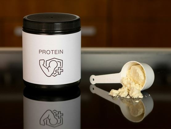Container of protein powder with a filled scoop spilled onto a reflective surface.