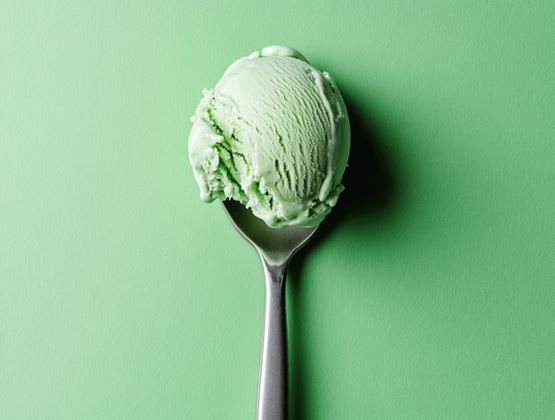 Scoop of green ice cream presented on a spoon against a matching green background.