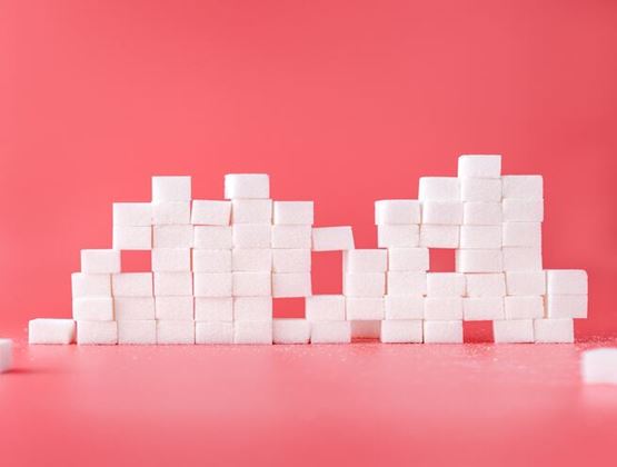 Morceaux de sucre blanc empilés en blocs sur un fond rose.