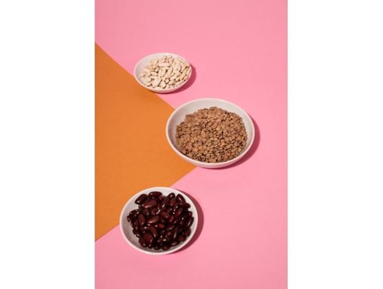 Bols de haricots blancs, de lentilles et de haricots rouges disposés sur un fond rose et orange.