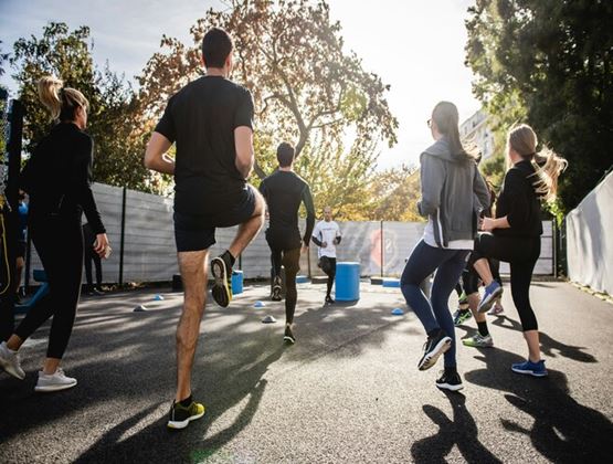 Groupe de personnes participant à une séance d’entraînement en plein air, sous la direction d’un coach, dans un espace urbain ensoleillé.