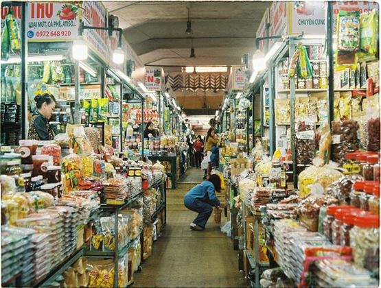 Allée étroite d’un marché couvert animé, bordée d’étals proposant des produits emballés, des épices et des aliments séchés.