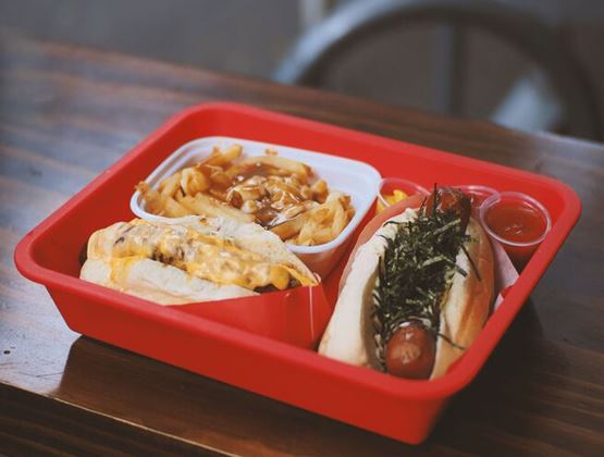 Plateau rouge composé de deux hot-dogs, de frites nappées de sauce et de petits récipients de condiments.