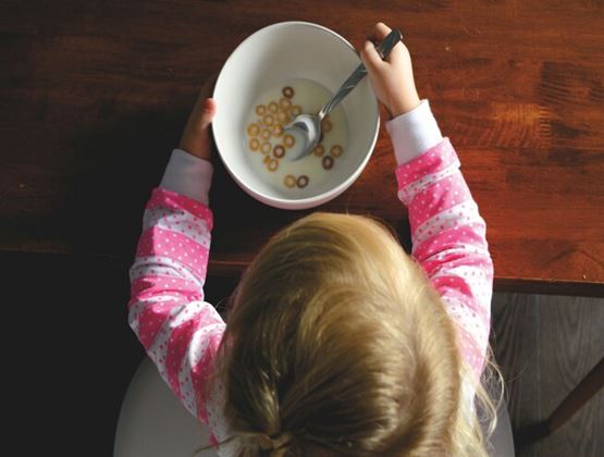 Overhead view of a child eating cereal with milk from a bowl at a wooden table.
