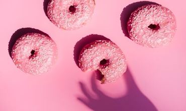Pink-glazed doughnuts topped with coconut flakes arranged on a pink background.