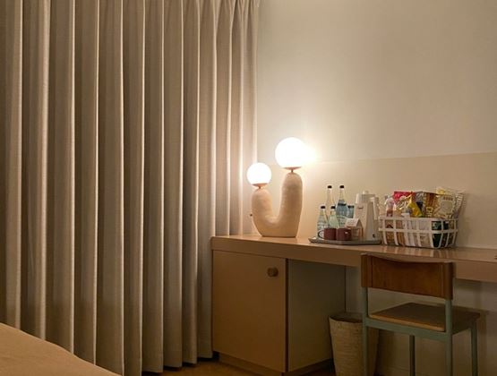 Espace minibar d’une chambre d’hôtel avec bouteilles d’eau, boissons et snacks emballés disposés à côté de lampes décoratives.
