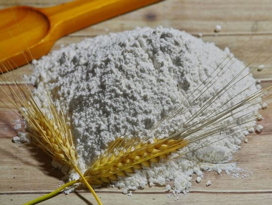 Tas de farine avec des épis de blé et une cuillère en bois sur une surface rustique