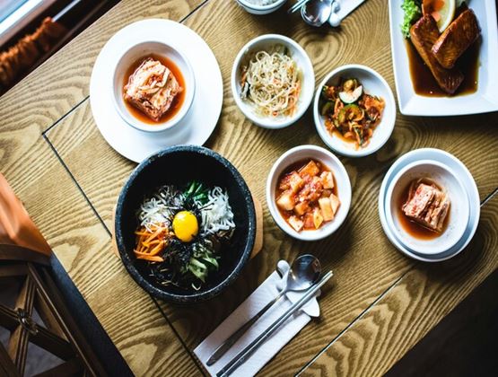 Korean dishes and side dishes arranged on a wooden restaurant table, including bibimbap and kimchi.