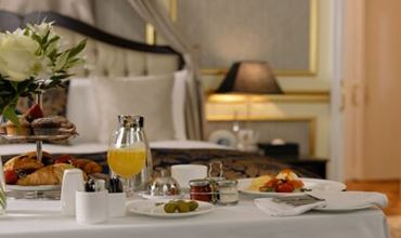 Petit-déjeuner en room service avec viennoiseries, fruits, jus d’orange et boissons chaudes disposés sur une table.