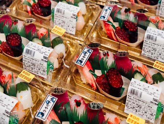 Assortiment de plateaux de sushis emballés avec étiquettes japonaises présentés à la vente en supermarché.