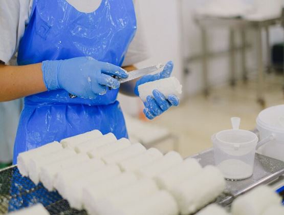 Employé de production alimentaire portant des gants et un tablier de protection préparant des blocs de produit alimentaire blanc.