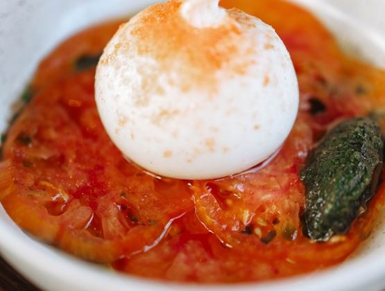 Burrata servie sur des tomates tranchées avec du pesto de basilic dans un bol blanc.