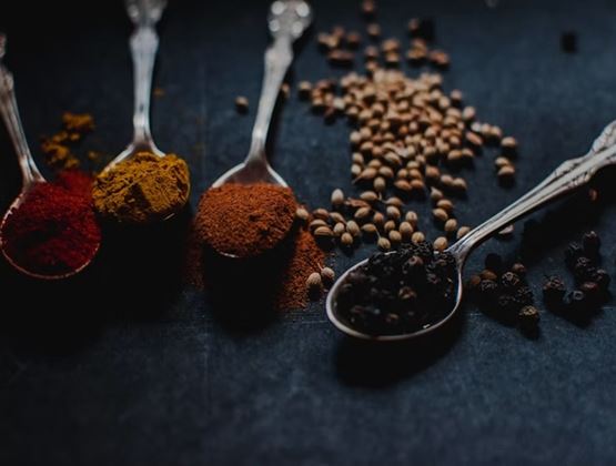 Assortment of spices and seeds displayed in spoons on a dark surface.