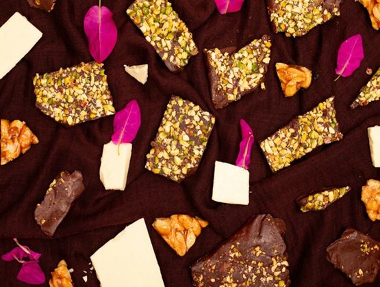 Assortiment de confiseries au chocolat et à la pistache avec morceaux de caramel et pétales décoratifs sur fond sombre.