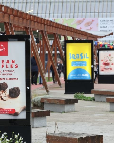 Affichage extérieur du salon SIAL Paris avec des panneaux publicitaires internationaux, des bancs en bois et une structure en bois moderne.