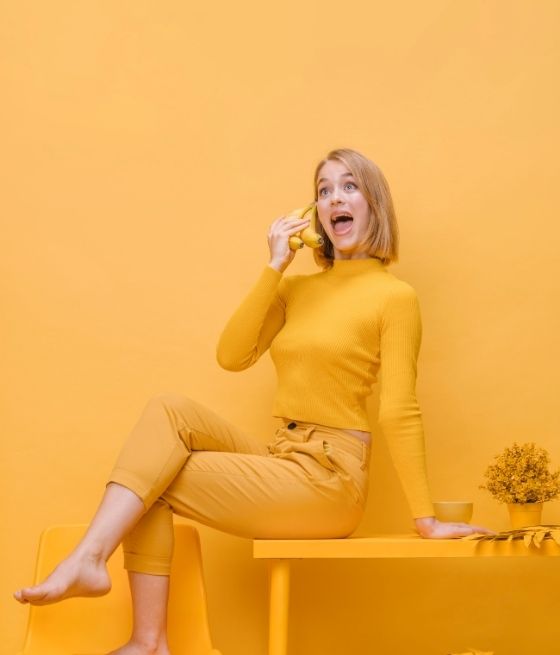 Femme assise vêtue de jaune, tenant un citron comme téléphone sur fond monochrome jaune.