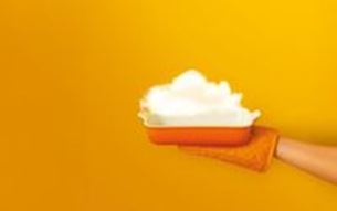 Hand holding a tray with white foam, on a solid yellow background.