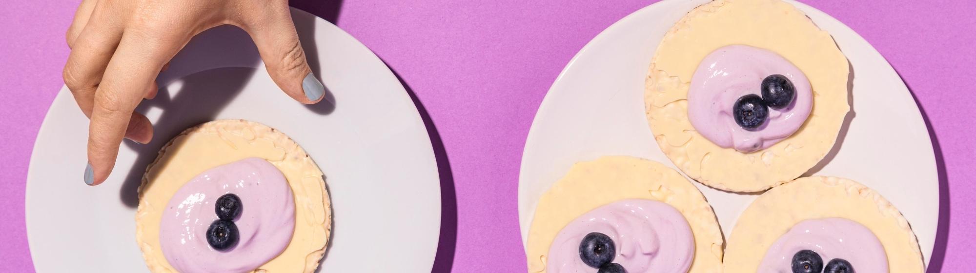 Desserts ronds garnis de crème et myrtilles sur fond rose, main prenant une pâtisserie