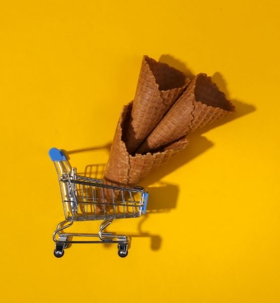 Cornets de glace placés dans un mini caddie sur fond jaune, composition ludique et minimaliste