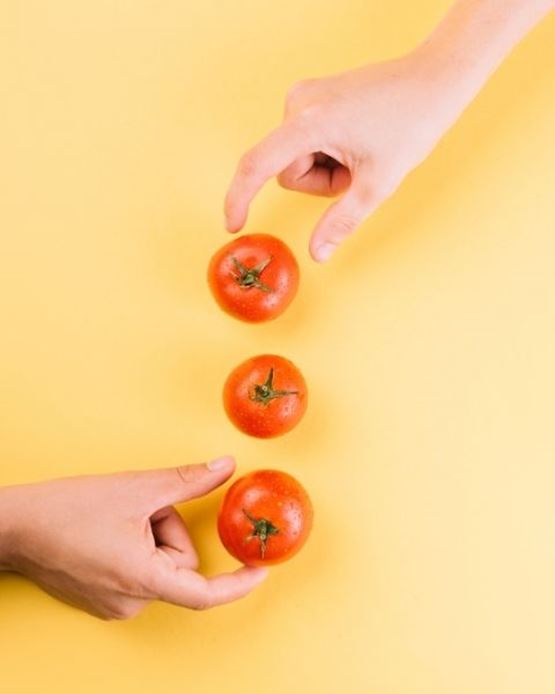 Trois tomates alignées verticalement sur fond jaune, mains les positionnant avec précision