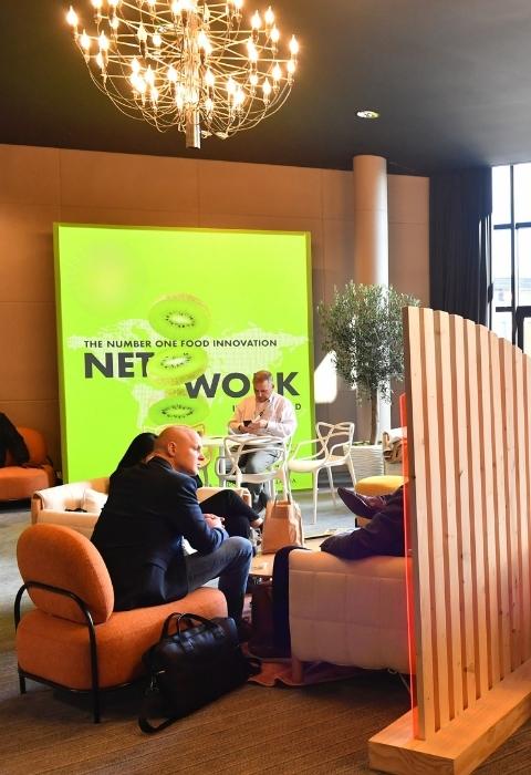 Personnes assises et discutant dans un espace lounge moderne avec grand écran SIAL vert en arrière-plan.