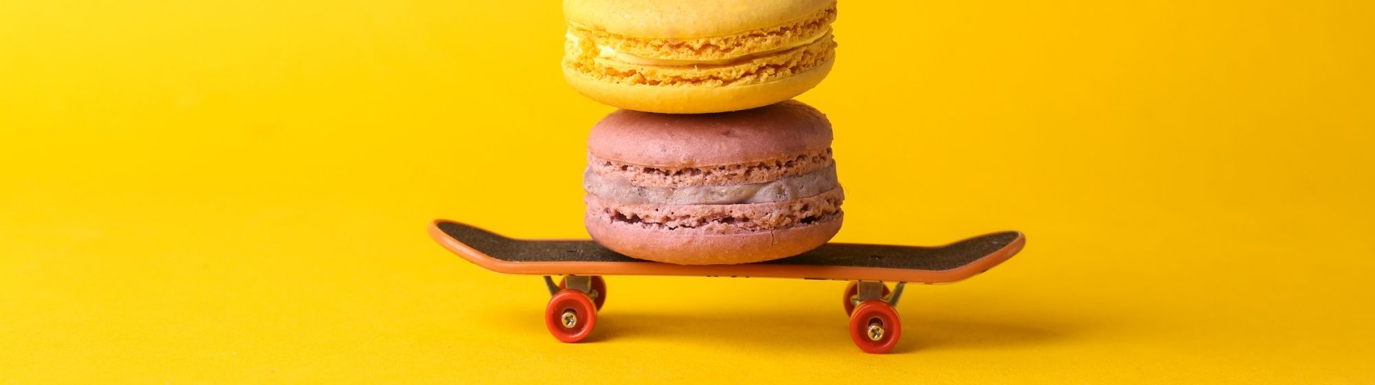 Deux macarons empilés sur un skateboard miniature orange, placés sur un fond jaune vif.
