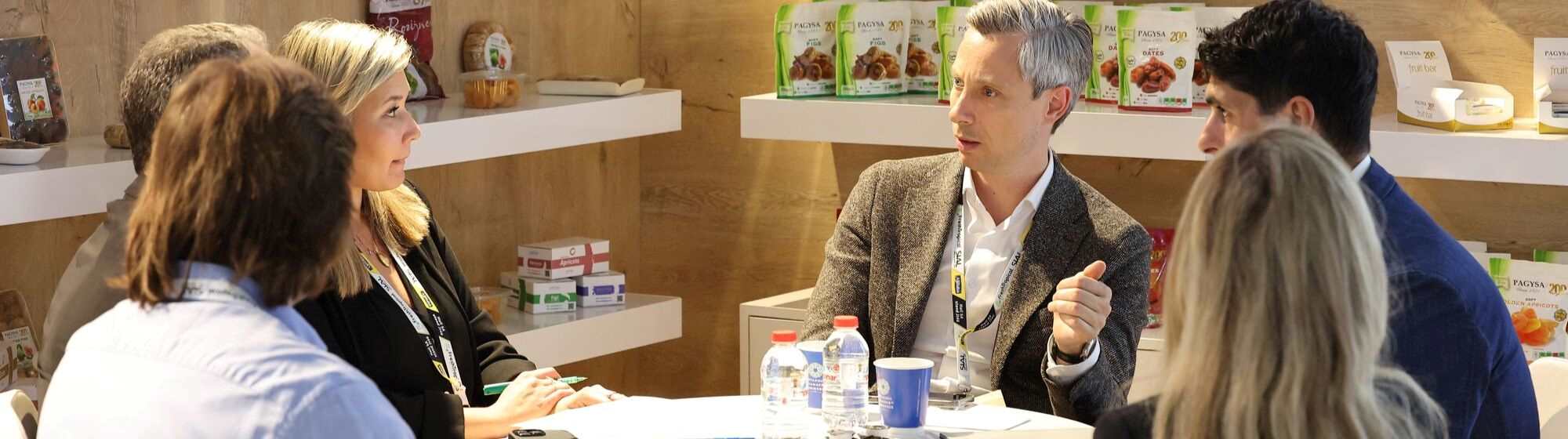 Group of professionals discussing around a table at a trade show, surrounded by displayed products.