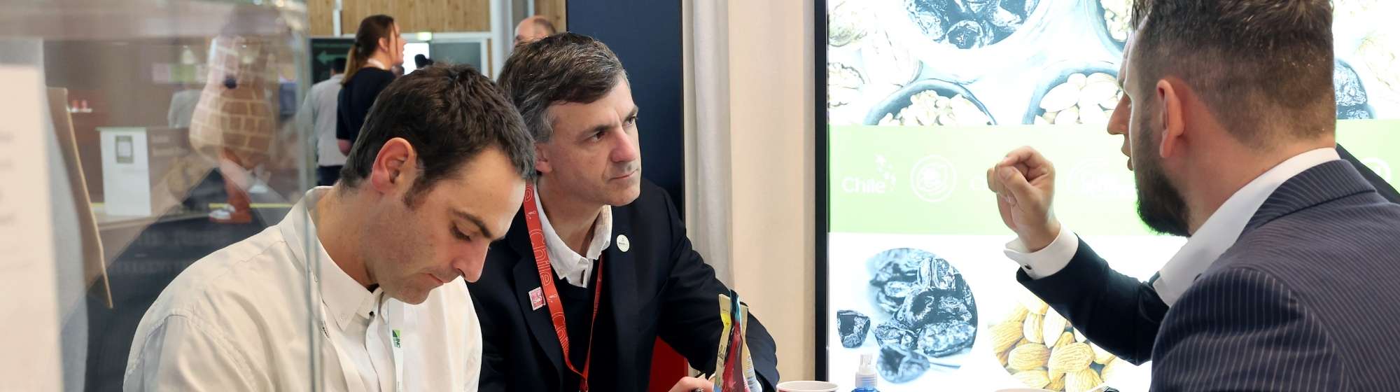 Trois professionnels échangent sur un stand devant un écran présentant des ingrédients alimentaires.
