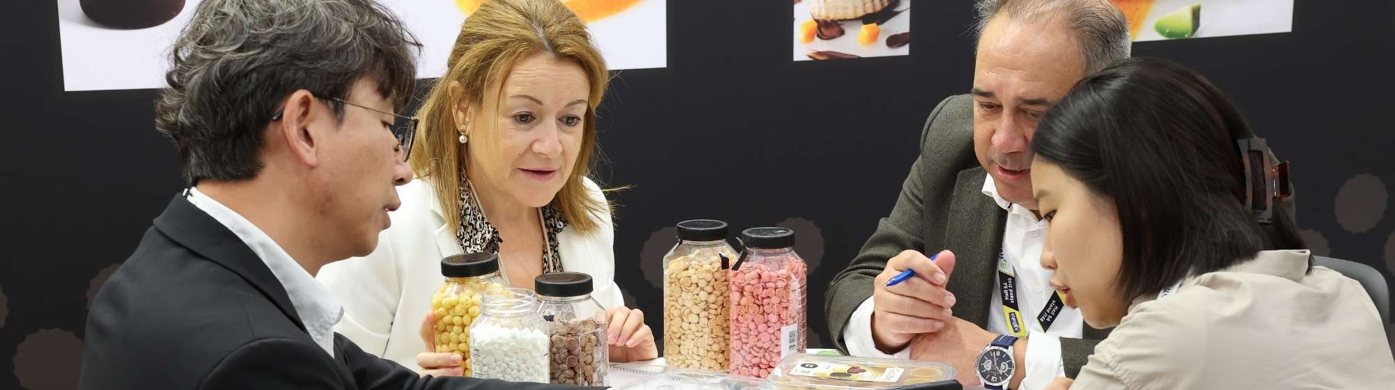 Quatre professionnels examinent des échantillons sucrés autour d’une table de réunion sur un stand.