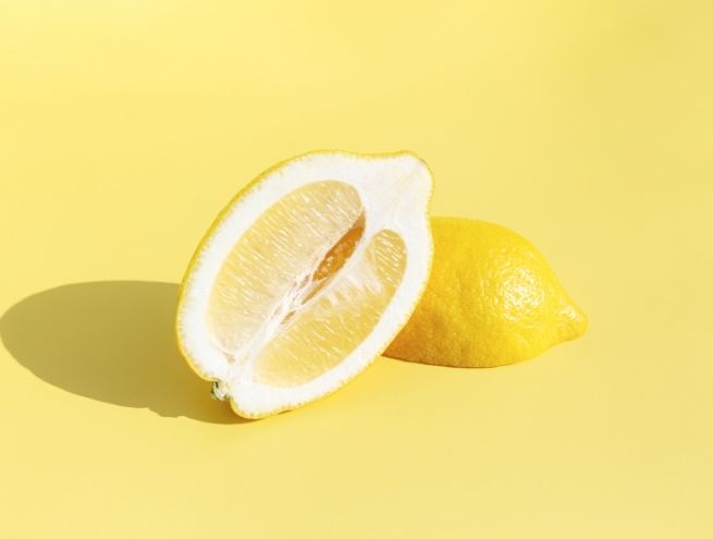 Demi citron coupé posé devant un citron entier sur fond jaune, éclairage studio minimaliste avec ombre douce