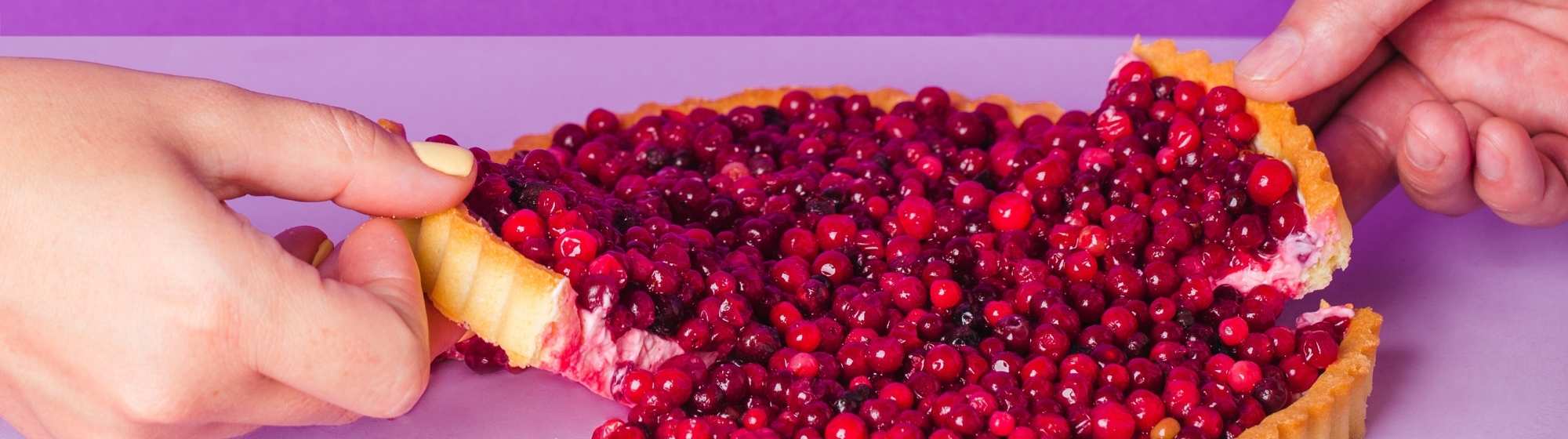 Two hands cutting a tart topped with glossy red berries, colorful and indulgent dessert scene