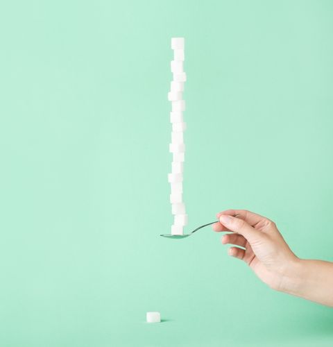 Sugar cubes stacked on a spoon held by hand, minimal composition on green background