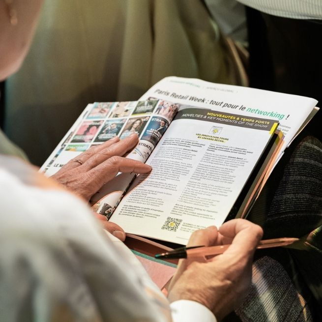 Personne feuilletant un catalogue pendant l'événement Paris Retail Week, avec des informations sur les nouveautés du salon.