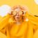 Senior woman wearing a yellow sweater and round glasses against a bright yellow background.