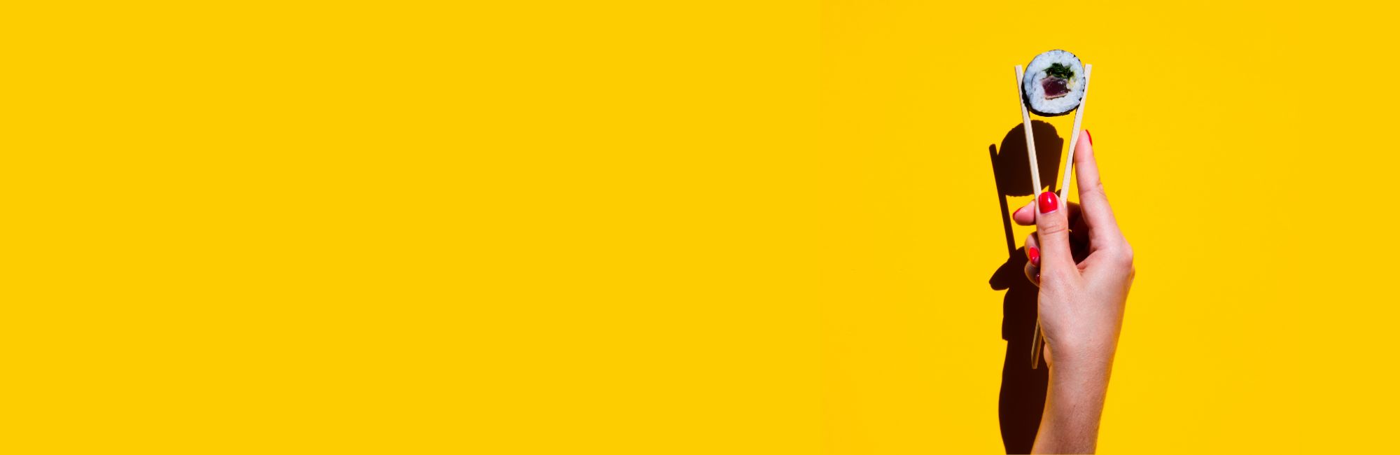 Main avec vernis rouge tenant un sushi avec des baguettes sur fond jaune vif avec grand espace vide.