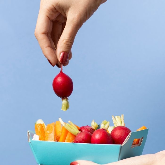 Tray of raw vegetables with radishes and vegetable sticks, held by hand