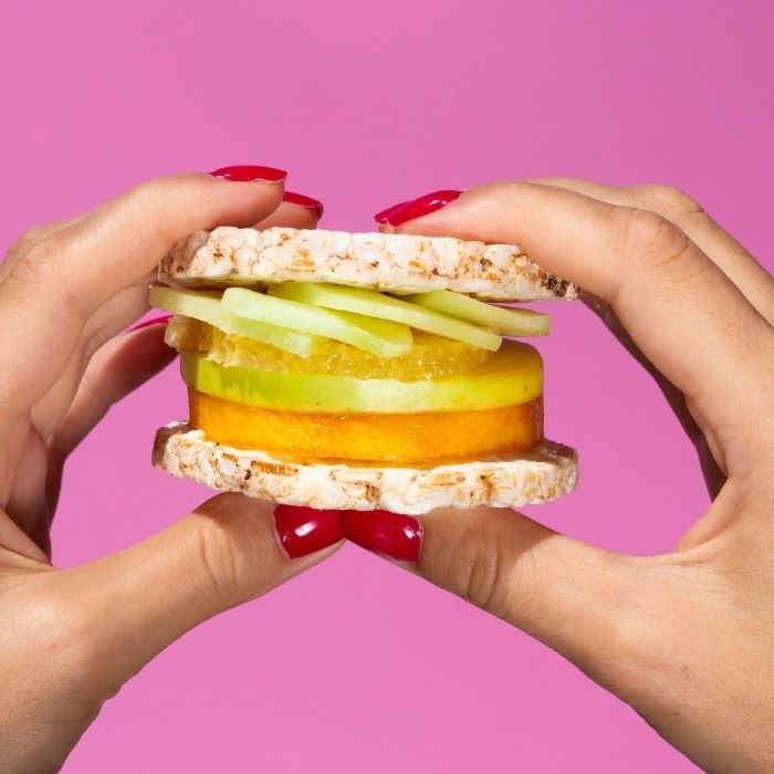 Sweet sandwich made with rice cakes filled with fresh fruit, held between two hands