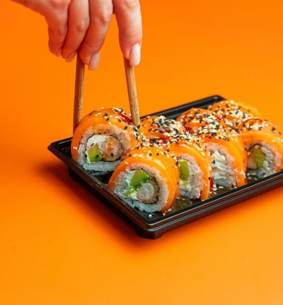 Plateau de sushis au saumon saisis avec des baguettes sur fond orange