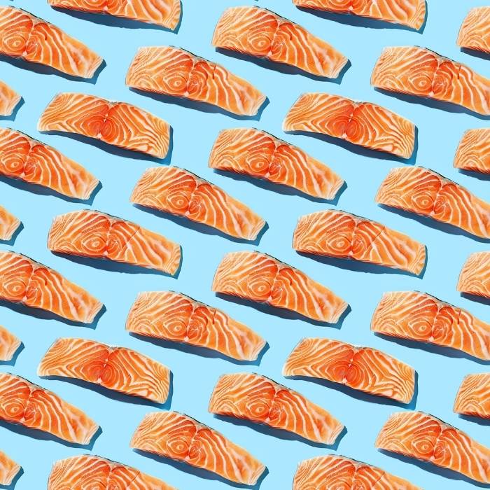 Raw salmon fillets arranged in a repeating pattern on a light blue background