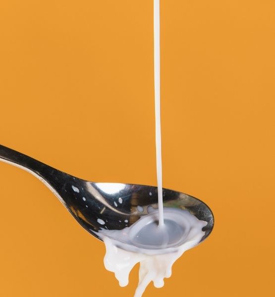 Lait liquide versé dans une cuillère en métal sur fond orange