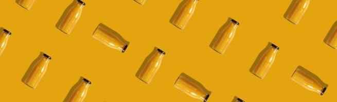 Répétition de bouteilles de jus orange disposées en diagonale sur un fond jaune.