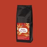 Sachet de café noir Cafés Henri avec étiquette festive rouge indiquant “Moka de Noël”, présenté sur fond rouge.