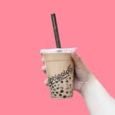 A hand holds a bubble tea with black pearls, against a pink background.