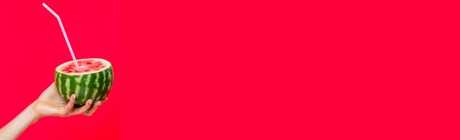 A hand holds a half watermelon with a straw, against a solid red background.