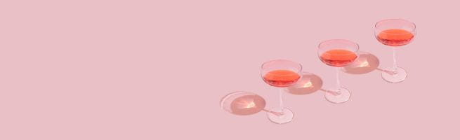 Trois verres à cocktail remplis d’un liquide rosé alignés sur fond rose.