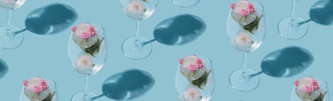 Verres à vin remplis de fleurs roses et blanches sur fond bleu, disposés en motif répétitif.