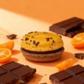 Large two-tone orange and chocolate macaron surrounded by mandarin slices and chocolate pieces.